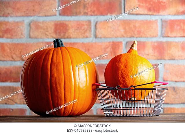 Two Autumn pumpkins and shopping basket on wooden table with brick wall at background