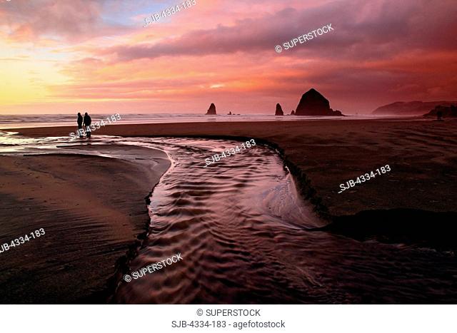 A couple at sunset, along Cannon Beach, Oregon. The Haystack right and the Needles are out in the surf