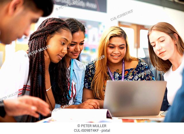 Female and male higher education students looking at laptop in college classroom