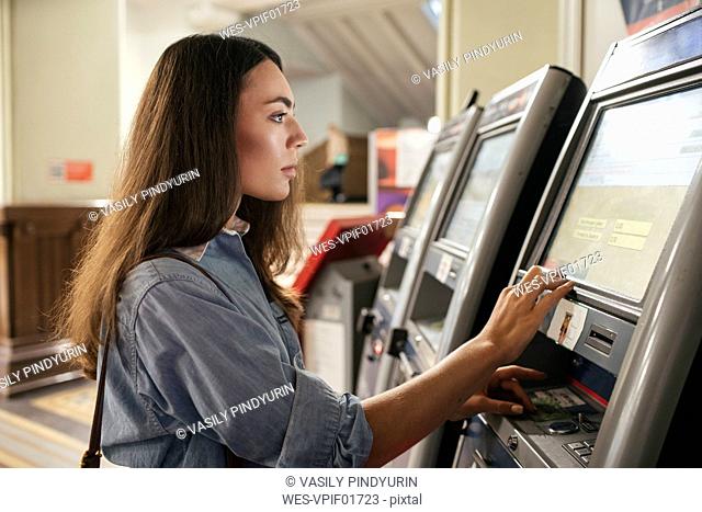 Young female traveller buying ticket from automated machine at station