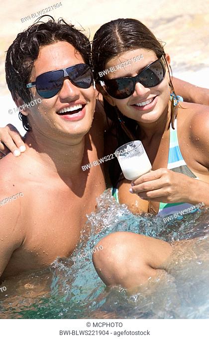 beautiful young couple in love having fun in a jacuzzi, wearing sunglasses and holding a cocktail