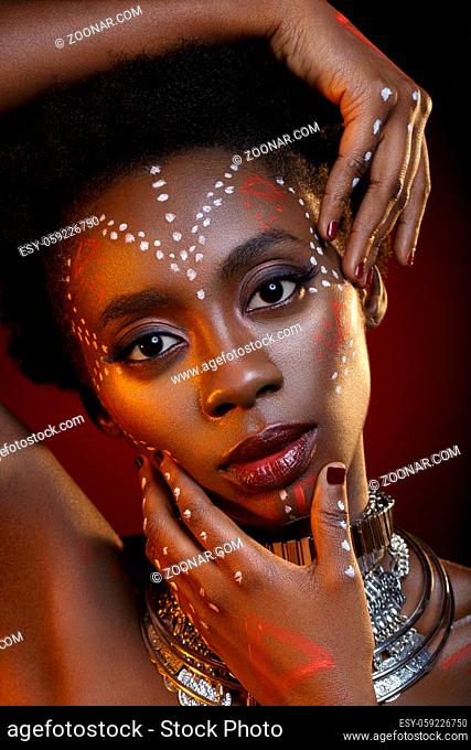 Beautiful young black woman with perfect skin and pink tone make up. Model with colourful crystal crown on head. Beauty shot on blue background