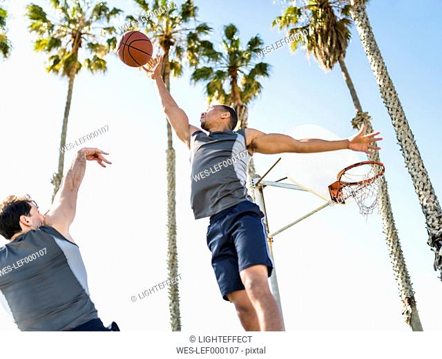 Two young men playing basketball on an outdoor court