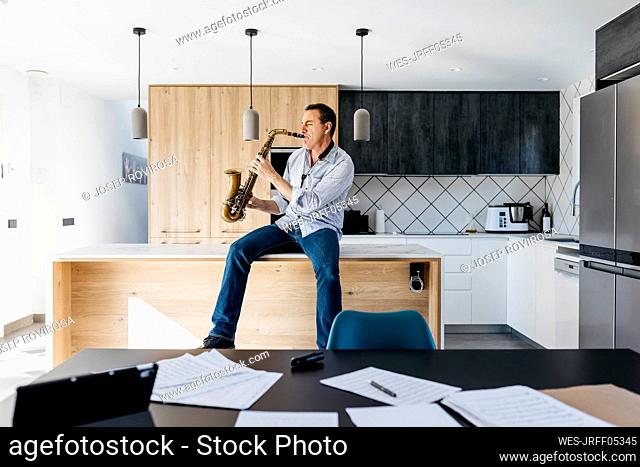 Musician with eyes closed playing saxophone sitting on kitchen island at home