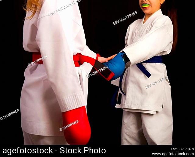 Two little karate women in white kimonos, one in red and the other in blue competition equipment shake hands as a sign of respect before the fight against a...