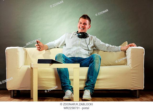man on couch with headphones smartphone and tablet