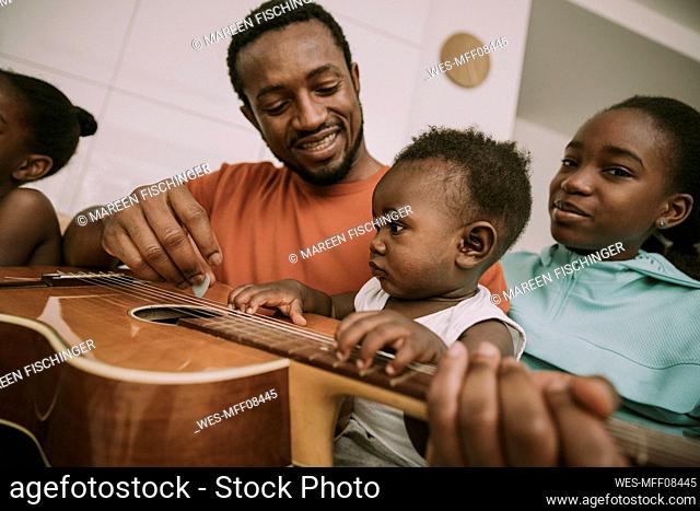 Father playing guitar by children at home