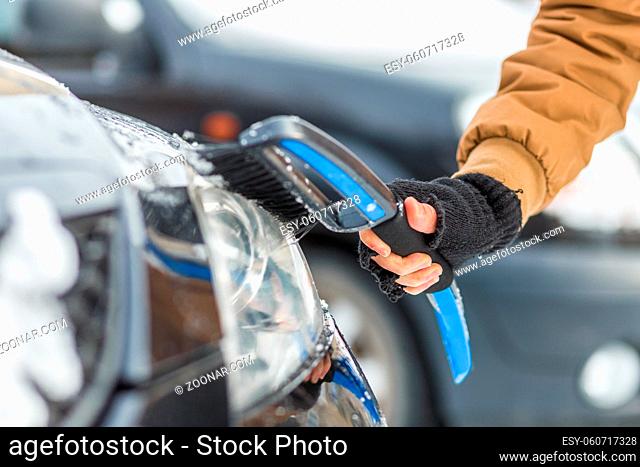 Vehicle and people concept - man cleaning snow from car with cleaning tool