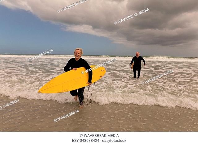 Senior couple running with surfboard on the beach