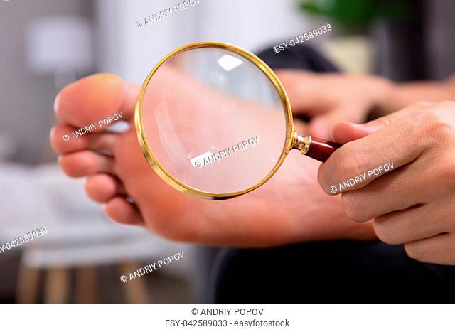 Close-up Of A Man's Hand Holding Magnifying Glass In Front Of His Feet