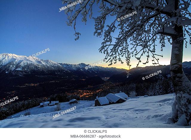 Lights of dusk illuminate the valley and the snow covered huts Tagliate Di Sopra Gerola Valley Valtellina Lombardy Italy Europe