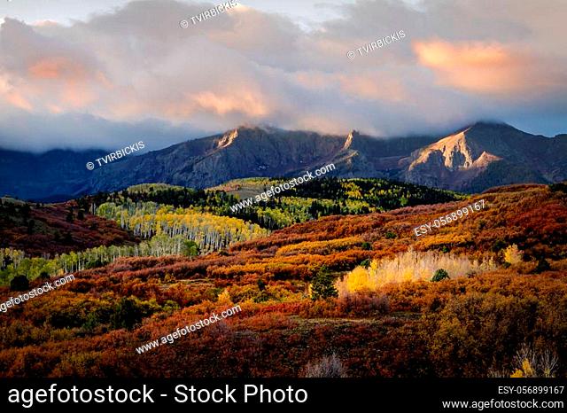 Close up of mountain peaks lit with early morning sunlight and dramatic clouds along Dallas Divide near Ridgway Colorado during full fall color in mountains
