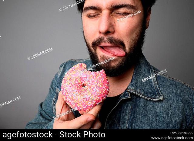 Hungry overweight man eating donuts isolated on grey background. High quality photo