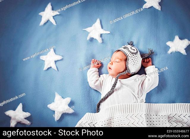 Cute newborn baby girl lying in the bed. 2 month old child in owl hat sleeping on blue blanket with stars