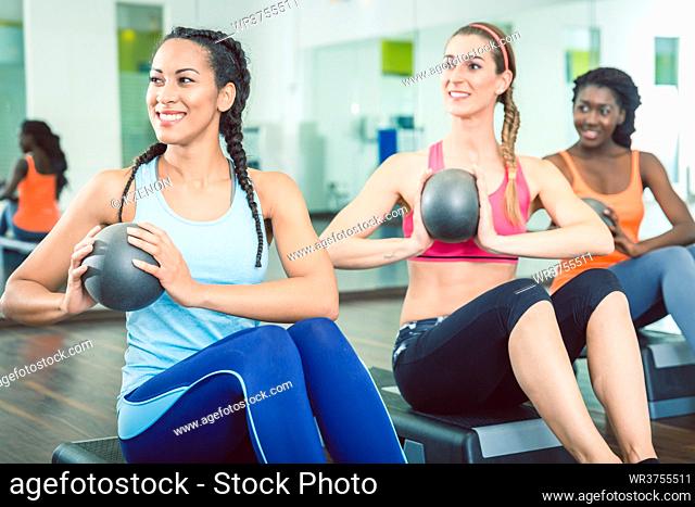 Beautiful young woman exercising Russian twist with med ball from sitting position for strong abs during group workout class for women at the gym