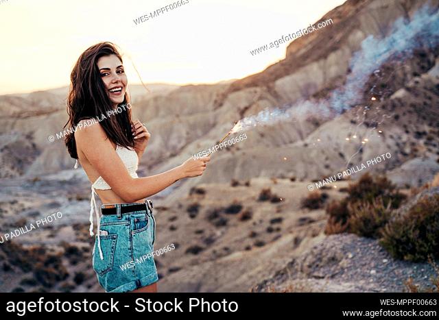 Portrait of happy young woman with sparkler at sunset, Almeria, Spain