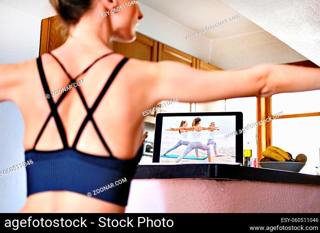 Woman rear back view practice yogic exercises Warrior 2 Pose or Virabhadrasana position watching on-line training on notebook screen repeat asanas