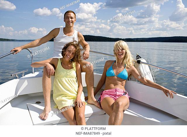 Two young women and young man sitting in yacht on lake