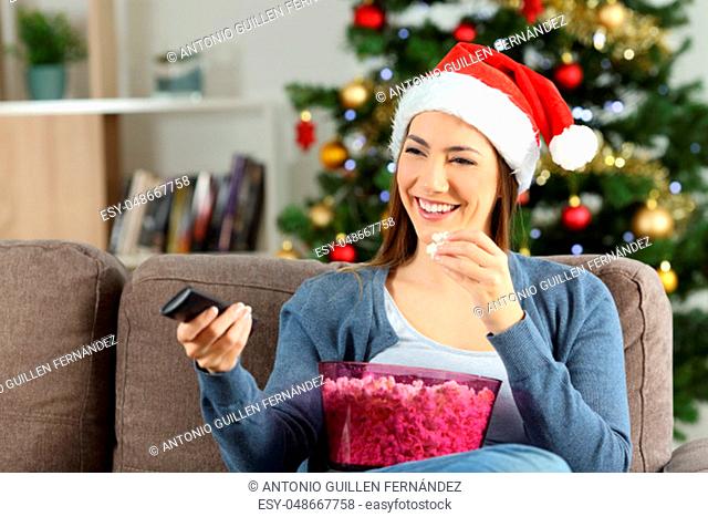 Happy woman watching christmas tv porgram sitting on a couch in the living room at home