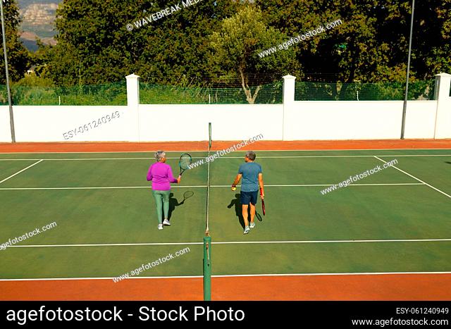 Rear view of biracial senior man with senior woman walking by net in tennis court during sunny day