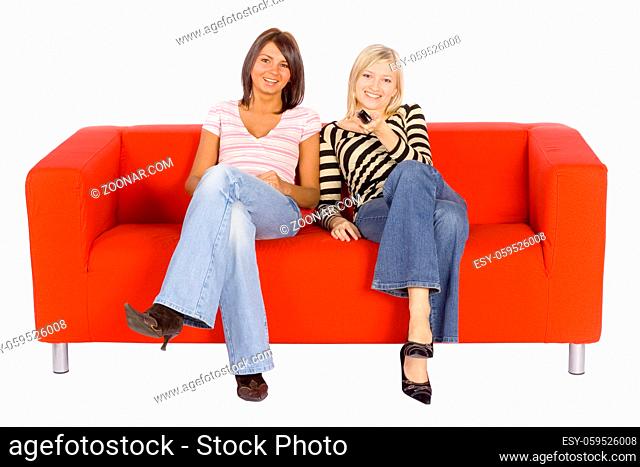 Two women sitting on a red couch with remote control. Isolated on white background, in studio