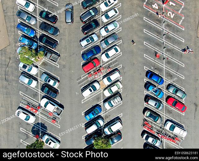 Aerial top view of parking lot at shopping mall with varieties of colored vehicles. People walking to their car and trying to park