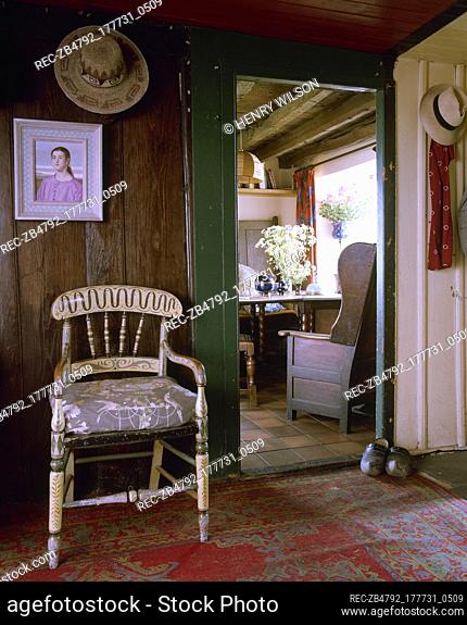 Rustic, country hallway with timber walls, weathered wood floor, painted craft chair, and an open doorway to an adjacent room