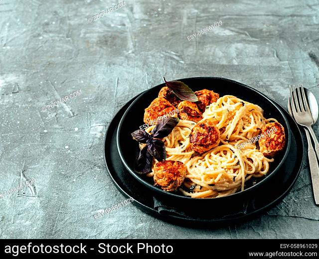 Zucchini Parmesan Meatballs with Pasta Carbonara in black craft plate over gray background. Close up view of creamy carbonara with copy space left