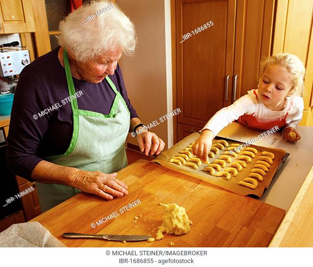 Grandmother and granddaughter baking Christmas cookies, girl putting dough onto baking sheet
