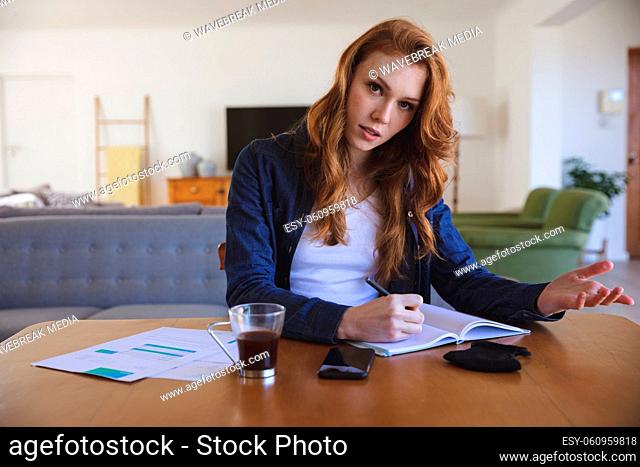 Portrait of a Caucasian woman spending time at home, in living room, working from home, writing in a