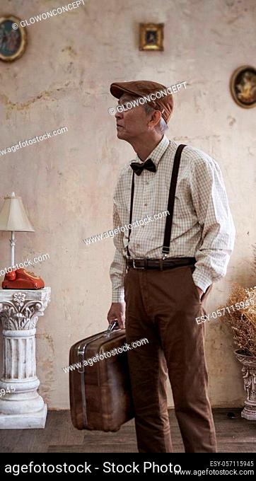 Retro vintage fashion Asian senior man with flat cap and suspender carry luggage for travel lifestyle