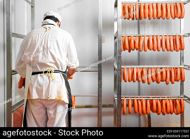 Worker hangs raw sausages on racks in storage room at meat processing factory. High quality photo