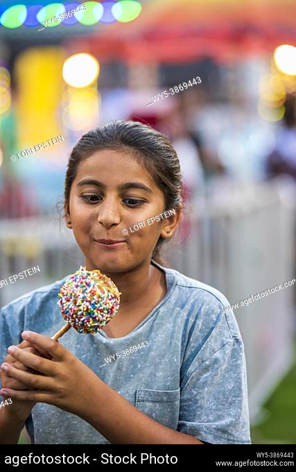 A 10-year-old girl eats a delicious caramel apple covered in sprinkles at a county fair in Arlington, Virginia