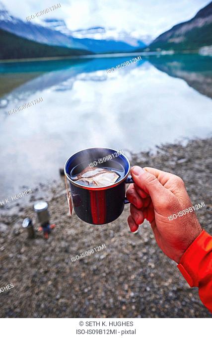 Cropped view of mans hand holding cup of tea by river, Banff, Alberta, Canada