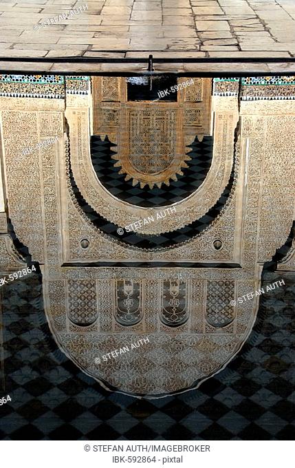 Reflection on water surface of oriental portal made of cedar wood with fine stucco richly decorated Medersa Ali Ben Youssef medina Marrakech Morocco