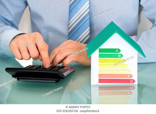 Businessman Using Calculator Near House Model Showing Energy Efficiency Rate