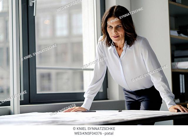 Businesswoman working in office, looking at blueprints