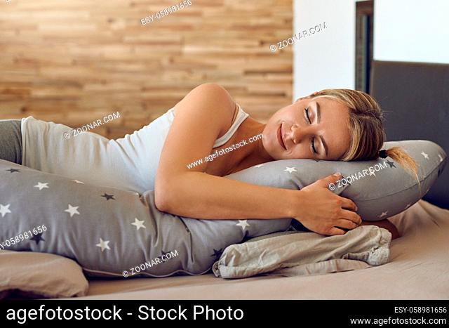 Pretty young pregnant woman sleeping using a special support cushion running the length of her body in a close up view with a peaceful serene expression