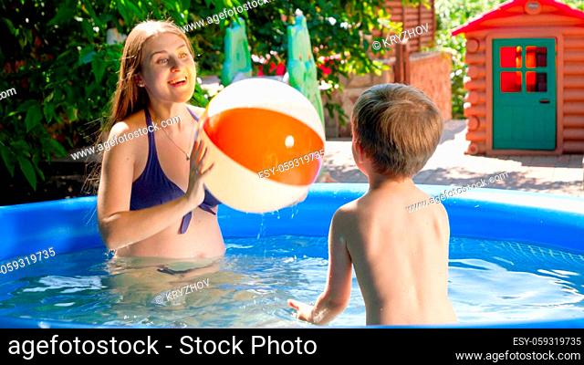 Happy smiling mother with little boy playing with beach ball in inflatable swimming pool on the house backyard. Family summer vacation and holidays