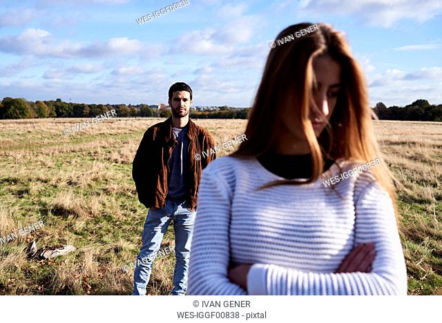 Serious young woman standing on a field with man behind her