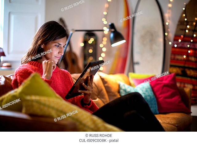 Young woman relaxing on living room sofa looking at digital tablet