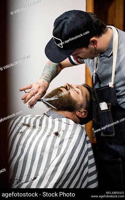 Barber trimming up clients beard in salon
