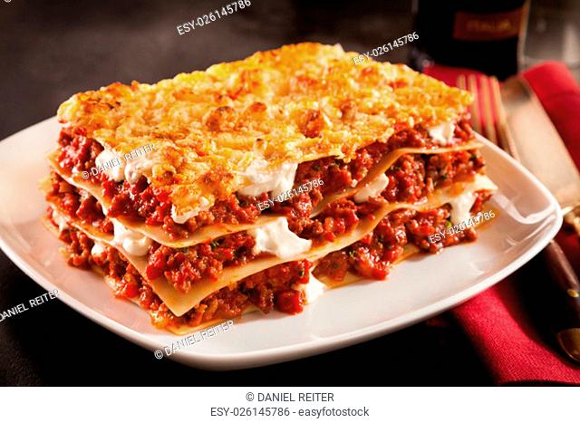 Serving of spicy traditional Italian beef lasagne in a restaurant on a modern white square plate with a red napkin, dark counter background