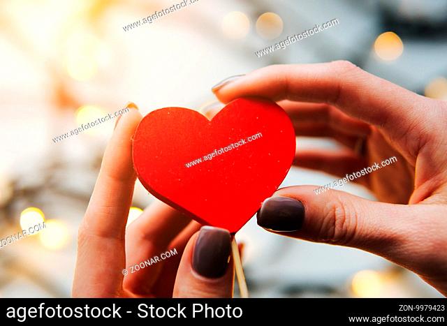 girl holding a red heart in the hands on the background of garlands