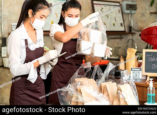 Asian waitress wear protective face mask prepare food for takeout and curbside pickup orders while city lockdown from coronavirus COVID-19 pandemic