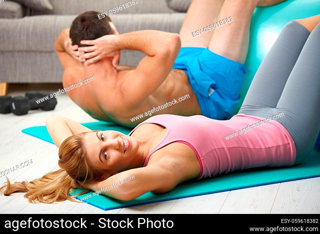 Young couple doing abdominal crunch using fit ball at home