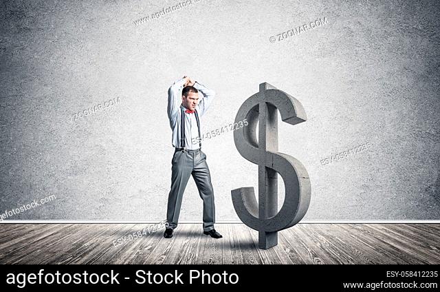 Young furious businessman going to crash with hands stone dollar symbol