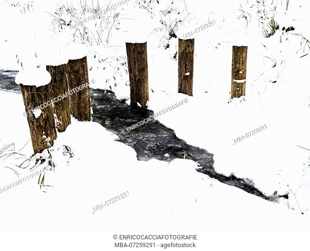 Dark creek on white snow with wooden posts