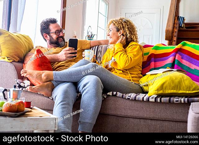 happy adult couple at home sitting on the sofa with colorful cover enjoy breakfast morning leisure activity together smiling and laughing with love and...