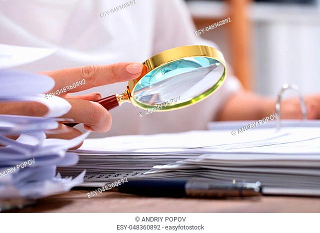 Close-up Of A Businesswoman's Hand Holding Magnifying Glass Over Invoice At Workplace